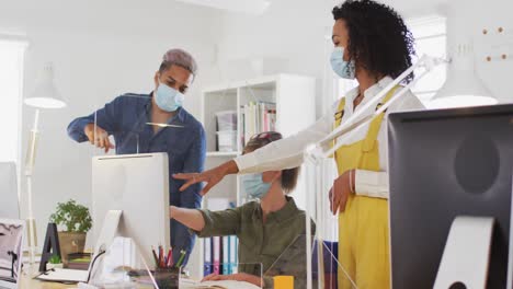 Office-colleagues-wearing-face-masks-discussing-over-computer-at-office