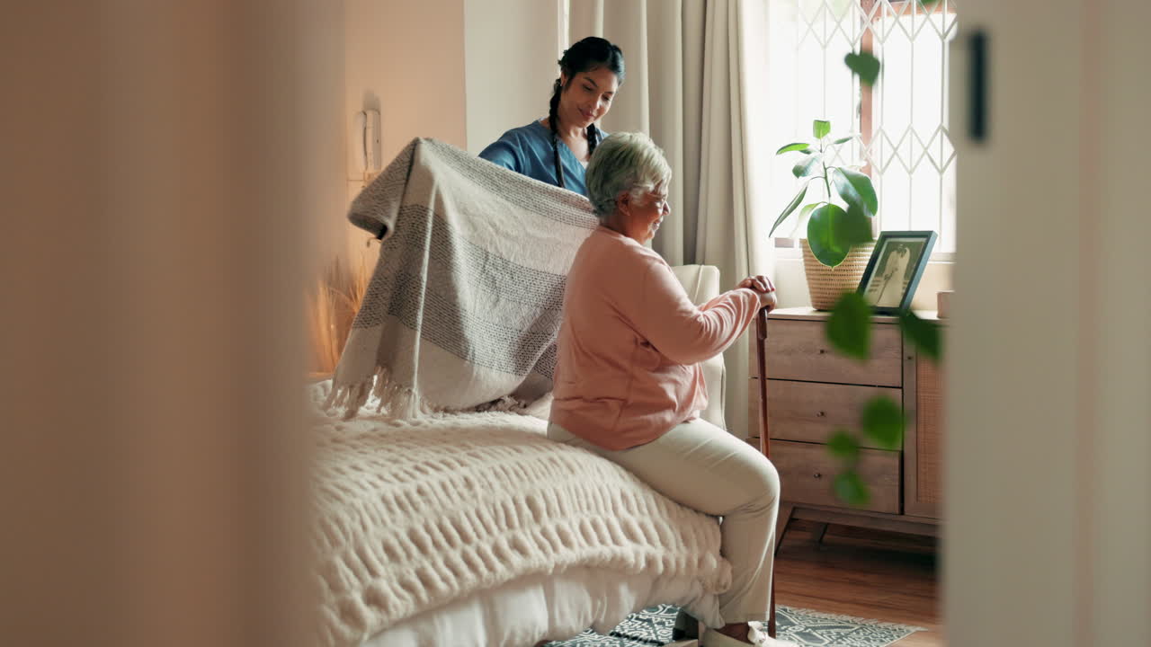 한 젊은 여성이 노인 여성이 침대에 앉을 수 있도록 도와줍니다.