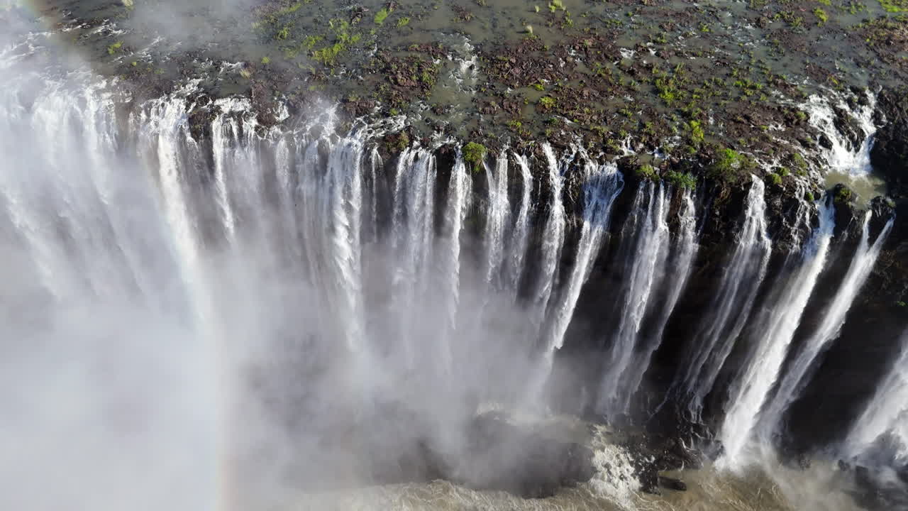 Aerial view of Victoria Falls with powerful waterfall plunging into gorge, mist rising above lush green forest, dramatic natural wonder and iconic travel destination in Africa