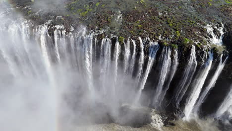 aerial view of victoria falls with powerful waterfall plunging into gorge, mist rising above lush green forest, dramatic natural wonder and iconic travel destination in africa
