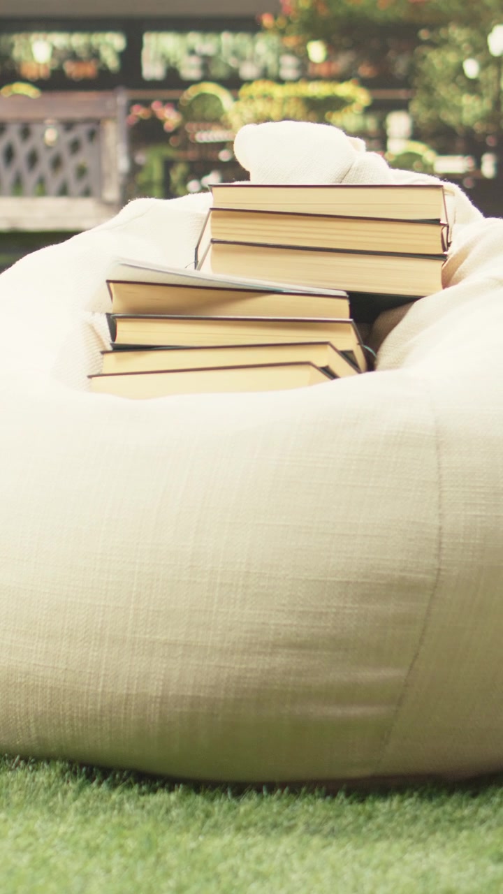 Vertical Video Stacks of books placed on beanbag on sunny campus lawn