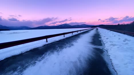 snow blowing across a beautiful promenade over a frozen lake during winter with mountains in the background during sunset in the appalachian mountains