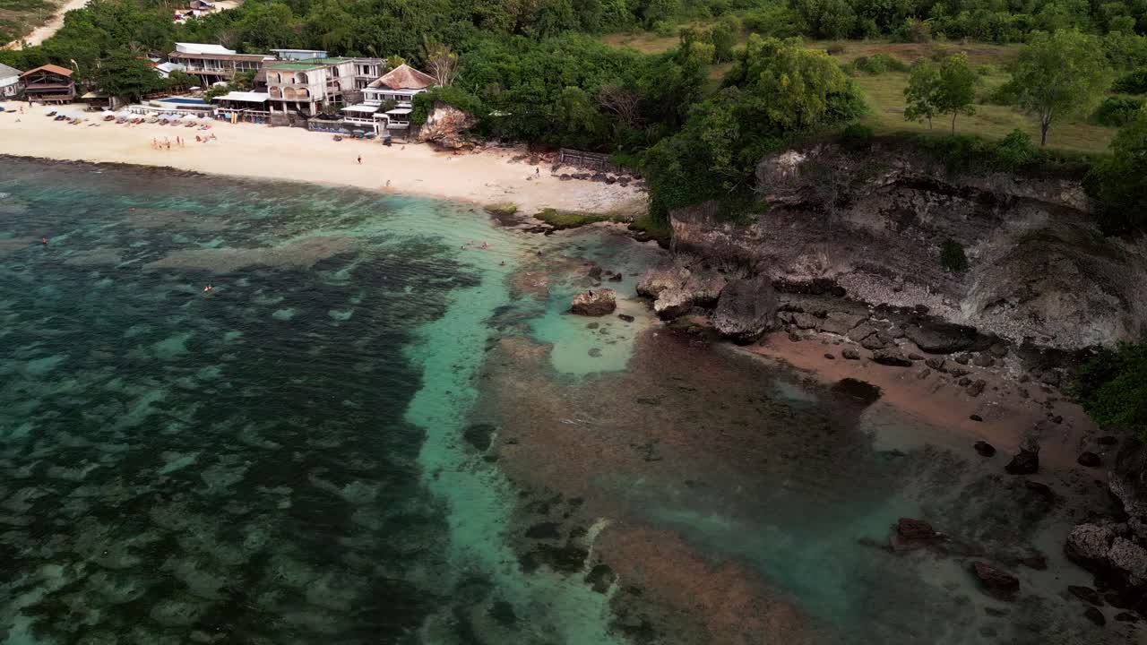 Drone view over Balangan Beach Bali showing turquoise reef channels cliff shoreline swimmers and snorkelers enjoying calm shallow water beside a sandy tropical bay with beach activity