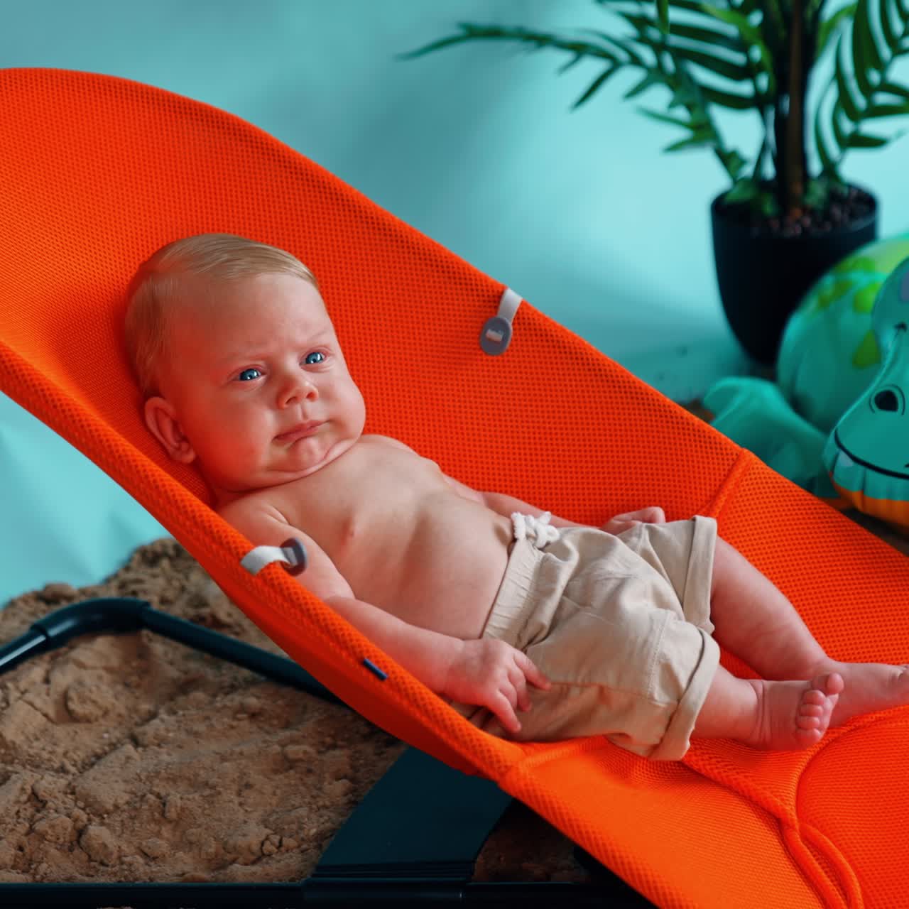 Blond tiny baby boy lying in the orange chair. Cute child resting at the improvised beach