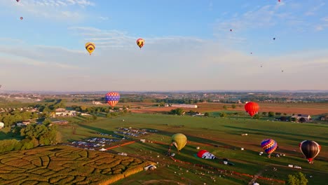 Vista-Aérea-De-Coloridos-Globos-Aerostáticos-Que-Se-Elevan-Hacia-El-Cielo-De-La-Mañana-Sobre-Un-Tranquilo-Paisaje-Rural