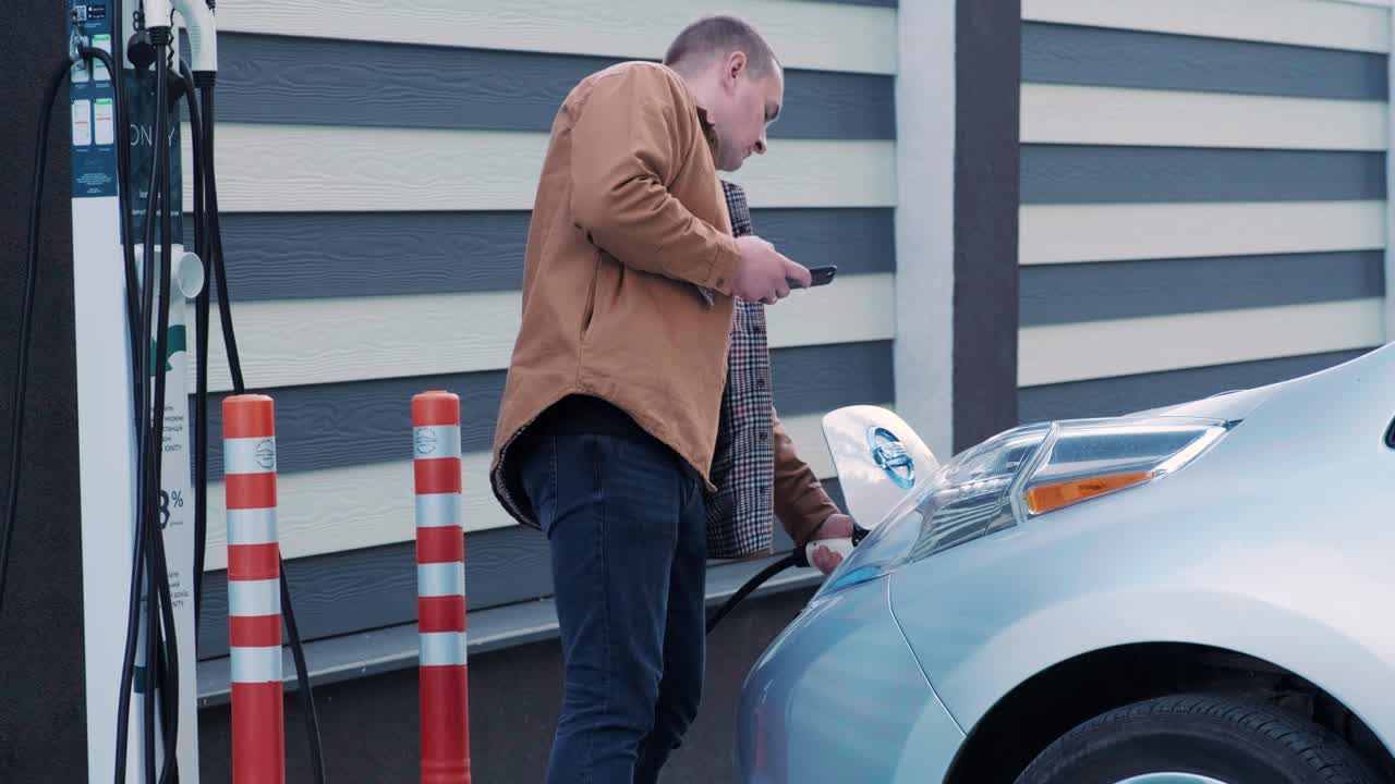 proceso de reabastecimiento de combustible de un automóvil eléctrico. un disparo debajo de la escotilla donde se carga el automóvil ecológico eléctrico. la escotella de carga del automóvil eléctrico se abre automáticamente. una mano masculina inserta un automóvil erecto
