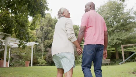 Happy-senior-african-american-couple-holding-hands-and-walking-in-garden,-slow-motion