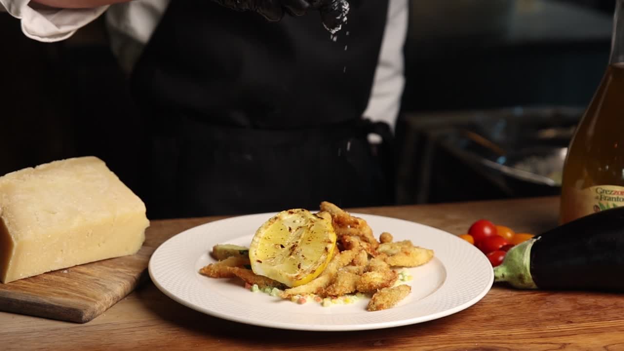 Chef che grattugia Parmigiano fresco su un piatto di frittura di pesce