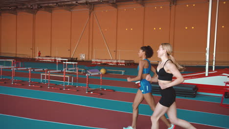 dos atletas femeninas multiétnicas corriendo juntas en una pista cubierta 2