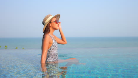 Classy-young-asian-sitting-in-shallow-water-of-infinity-swimming-pool-on-sunny-day,-exotic-caribbean-vacation-concept,-full-frame