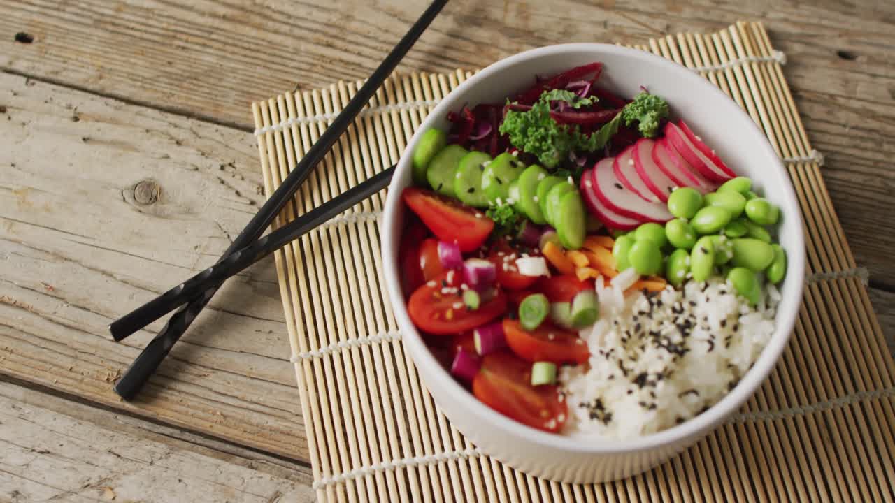 Composition of bowl of rice and vegetables with chopsticks on wooden background