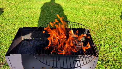 a barbecue grill ignites with vibrant flames while cooking outdoors in a sunny grassy area