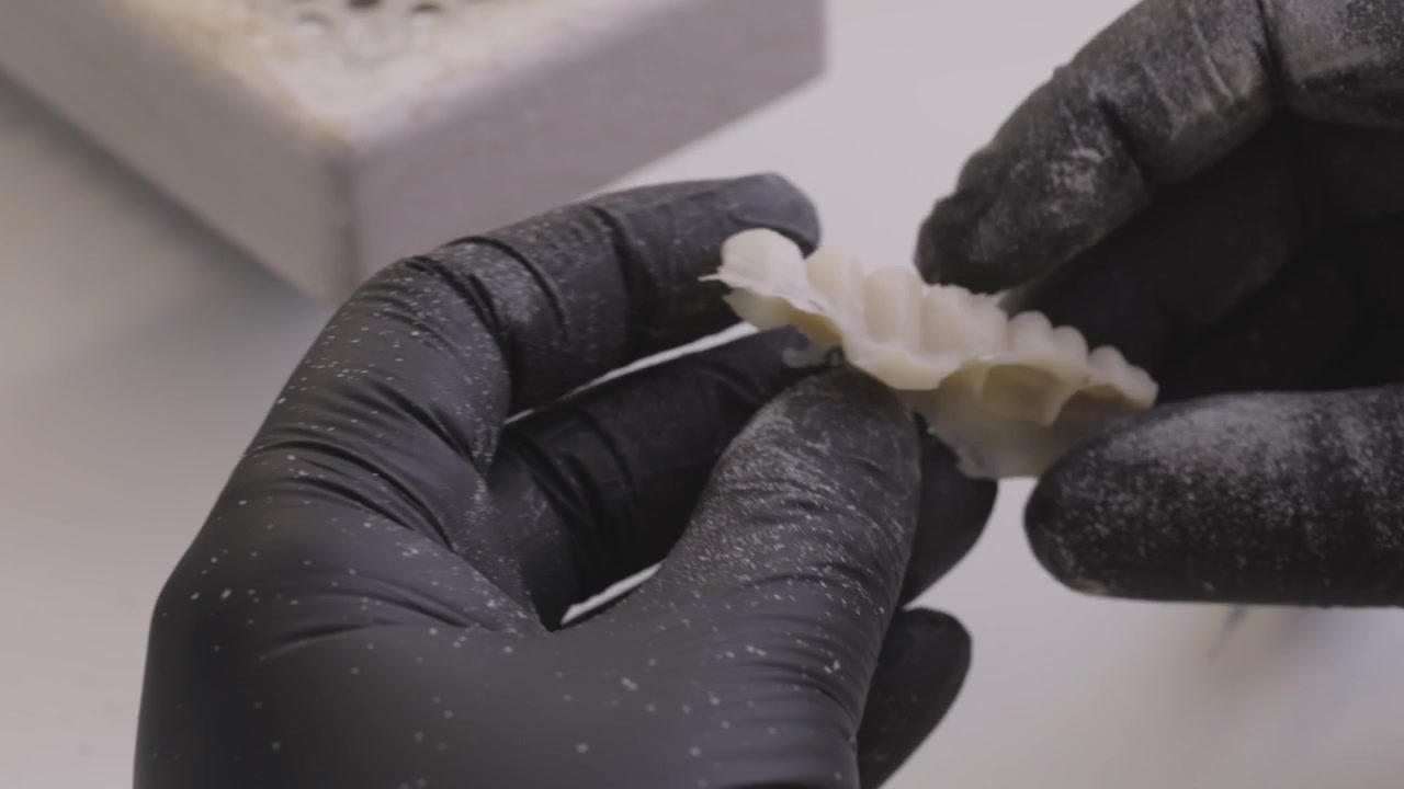 Close-up of black gloved hands crafting a dental veneer mold