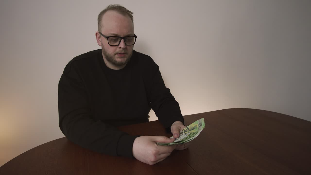 Ung man skakar på huvudet i besvikelse medan han räknar eurosedlar. Låg lön, ekonomiskt missnöje och stress över personlig budgetering