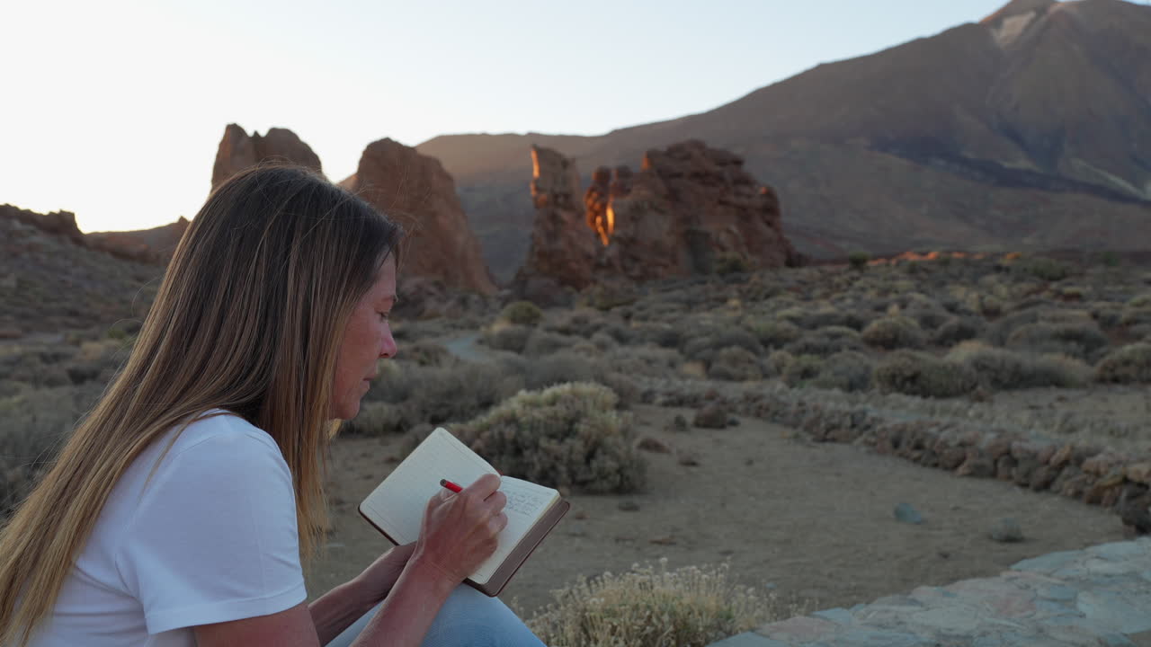 Viaggiatrice che annota i suoi pensieri circondata dallo splendido scenario vulcanico del Parco Nazionale del Teide durante un tramonto dorato a Tenerife