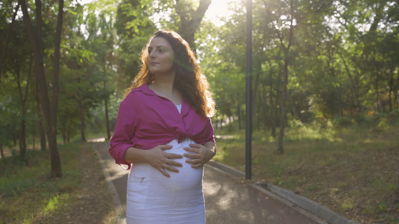 공원에서 혼자 걷는 임신한 여성 기대하는 어머니, 매력적인 백인 캐주얼 옷을 입은 엄마는 손을 편안하게 하고 배를 만지고 애무하는 애무, 가임기 부드러움, 중간 초상화 샷