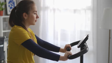 Joven-Deportista-En-Bicicleta-Estática-En-La-Sala-De-Estar-Entrenando-Sola-Durante-El-Fin-De-Semana-Equipo-Deportivo-Para-Hacer-Ejercicio-En-Casa-Mantenerse-En-Forma-Y-Perder-Peso