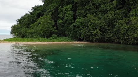 Luftaufnahme-Eines-Kaukasischen-Jungen-Mannes,-Der-In-Seinen-Schwarzen-Shorts-Am-Weißen-Sandstrand-Ins-Wasser-Rennt-Und-Hineintaucht-Und-Zu-Schwimmen-Beginnt