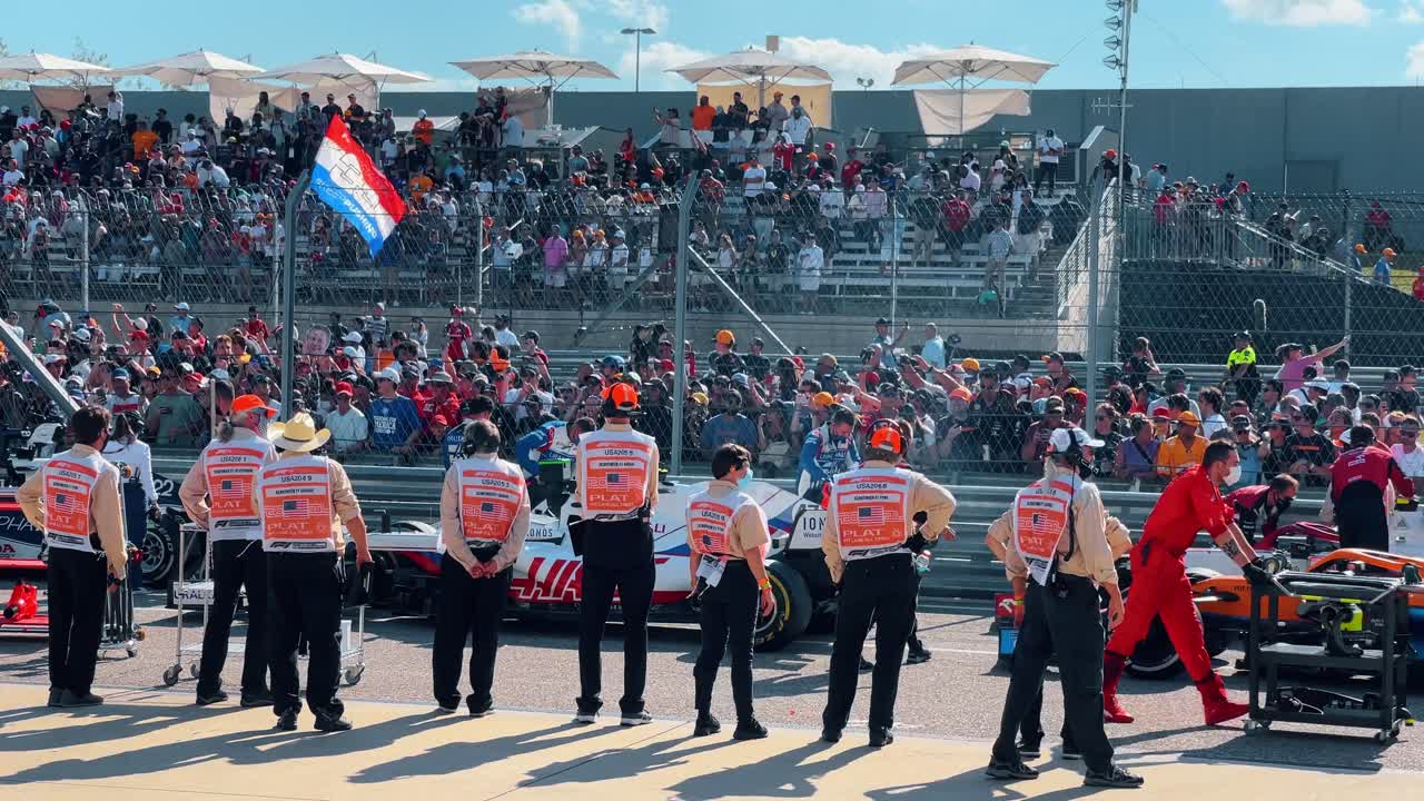 Austin, USA, 1 agosto 2022: Personale del circuito in piedi accanto all'auto sulla griglia dei box. Vista a livello del suolo dei membri del team con giubbotti in piedi accanto a un'auto da corsa bianca e rossa durante una competizione negli USA