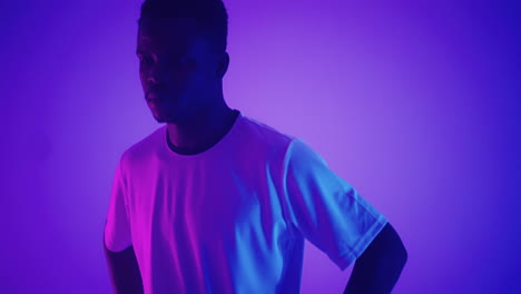 slow motion portrait of a black professional football player in a white uniform looking into the camera in the blue-red neon light of the studio. a brutal football player confident and victorious
