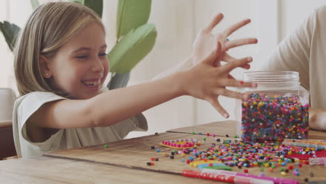 el primer plano de una hermosa niña rubia tirando cuentas de colores sobre la mesa y pasándola muy bien