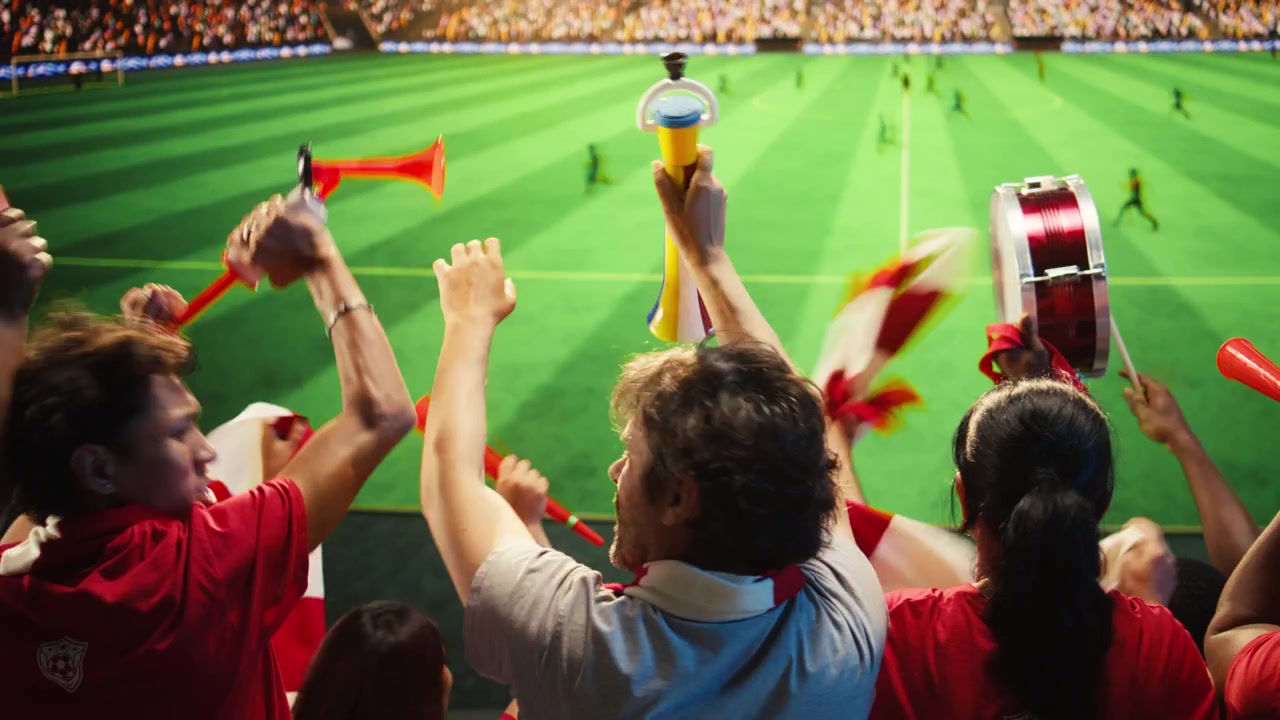 Aficionados al fútbol con camisetas rojas reaccionan con emoción a un gol anotado durante el partido