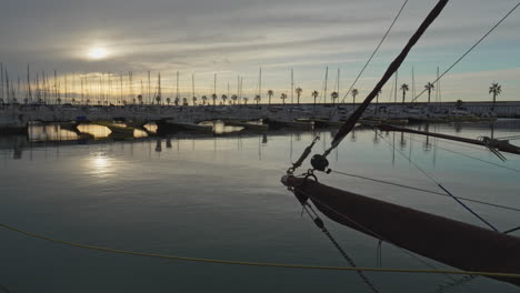 docked boats move in calm water as golden hour sun reflects in still sea