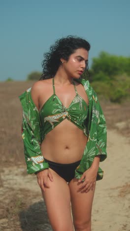 woman in green printed wrap top and black bikini bottom posing outdoors in sun
