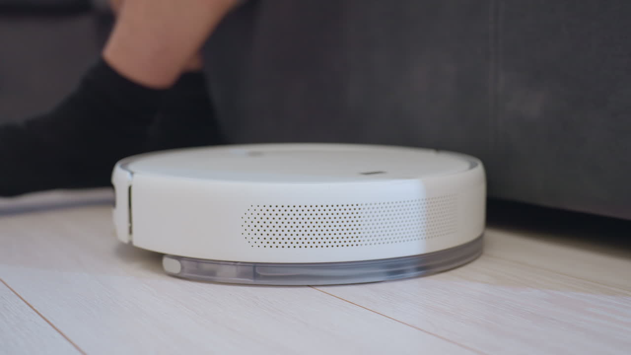 Robot vacuum rotates carrying bottle of drink while person nearby reaches to take it, showcasing futuristic smart home concept, creative lifestyle convenience and innovative household technology