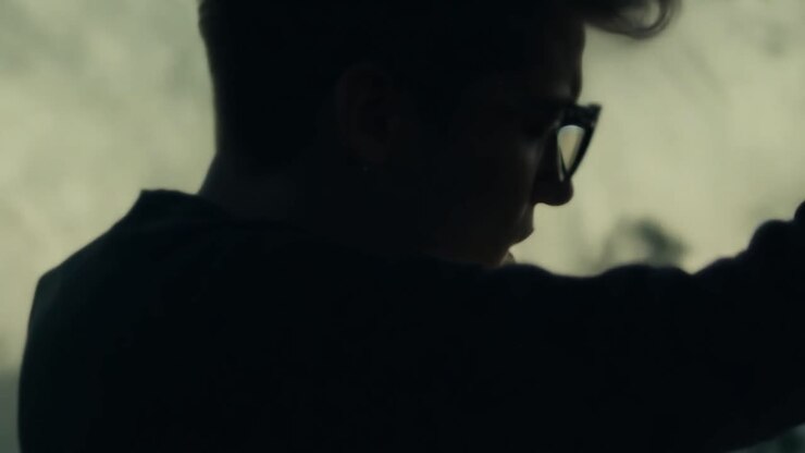 A man with sunglasses and an earring smoking a cigarette in the fog.