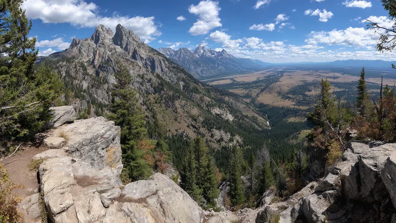 Vista Mozzafiato di un Maestoso Paesaggio Montano con Foresta Lussureggiante e un'Ampia Valle Sotto un Cielo Azzurro Splendente con Nuvole Bianche e Soffici