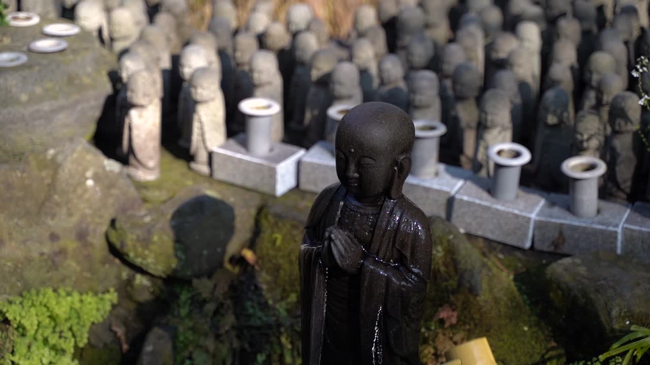 Female Hand Pouring A Buddha Statue With Numerous Buddha Figures In The Background - medium shot
