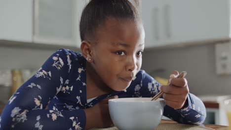 Chica-Afroamericana-Sentada-En-La-Encimera-Y-Desayunando-En-La-Cocina,-Cámara-Lenta,-Inalterada