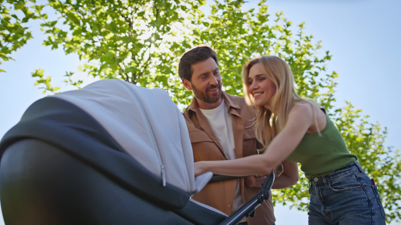Young parents carrying stroller crossing at sunny nature closeup. Happy couple