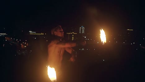 Young-blond-male-spins-two-burning-torches-at-night-Slow-motion-shot