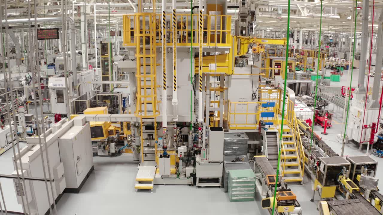 High-angle view inside a modern industrial plant with yellow platforms, conveyors and robots, showing large-scale automated manufacturing and assembly operations