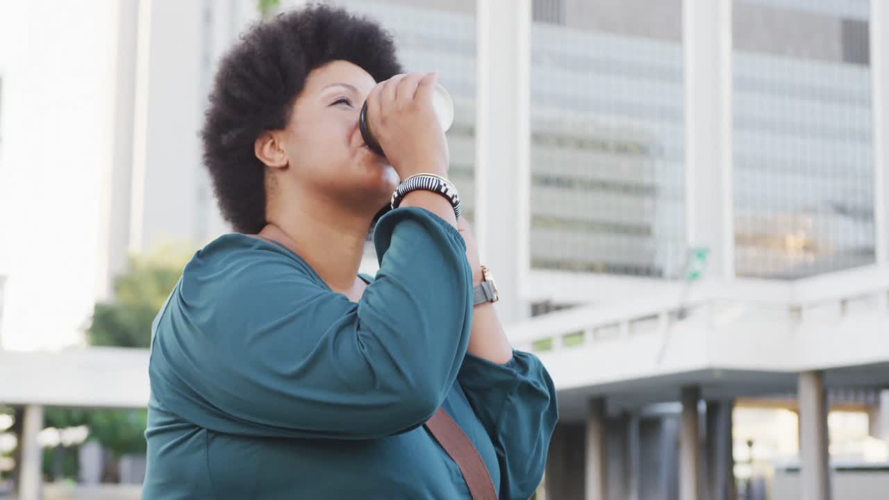 mujer biracial feliz de talla plus hablando en el teléfono inteligente y bebiendo café