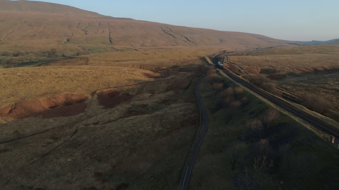 toma aérea de un dron siguiendo el tren en el puente del tren del viaducto ribblehead en un impresionante amanecer en verano en los valles de yorkshire, inglaterra, reino unido, panoramización a 3 picos de la montaña whernside