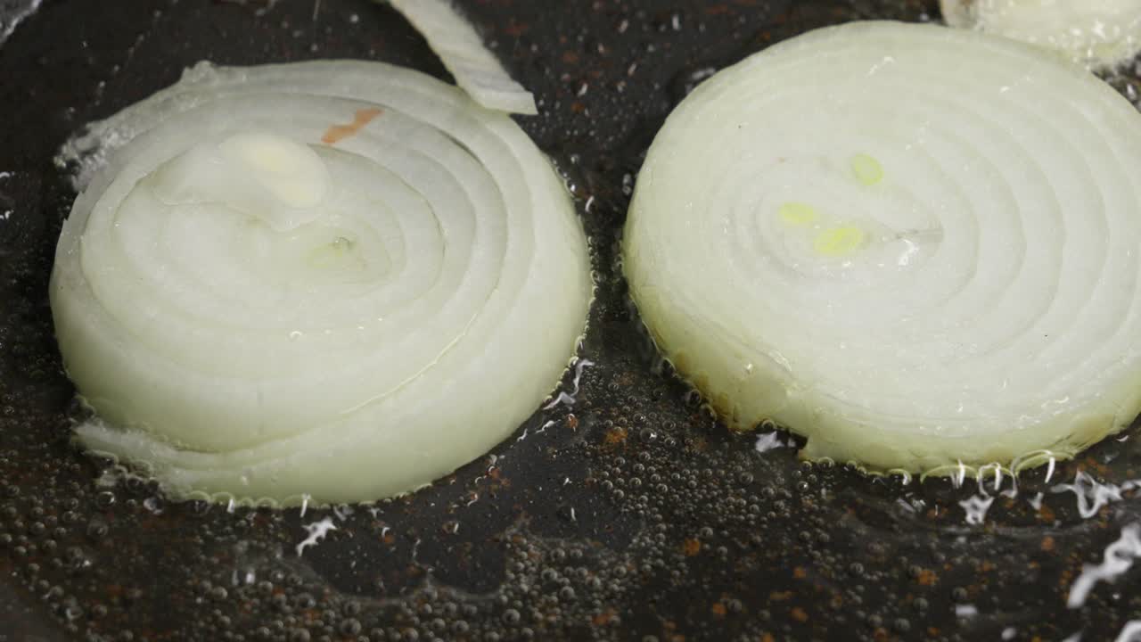 熱いフライパンでじゅうじゅうと音を立てる油で玉ねぎのスライスを炒めるクローズアップ