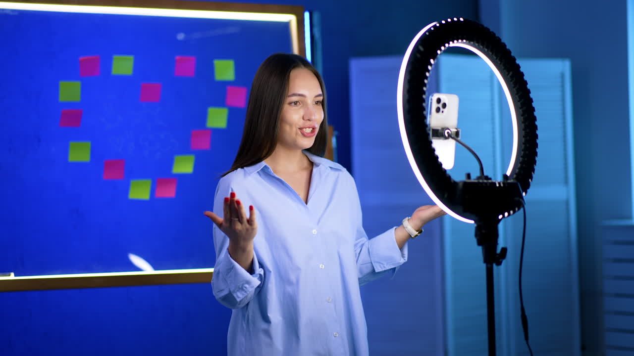 Woman speaking before colors. A woman speaks to an audience, using a ring light and colorful sticky notes as a backdrop, dressed in blue