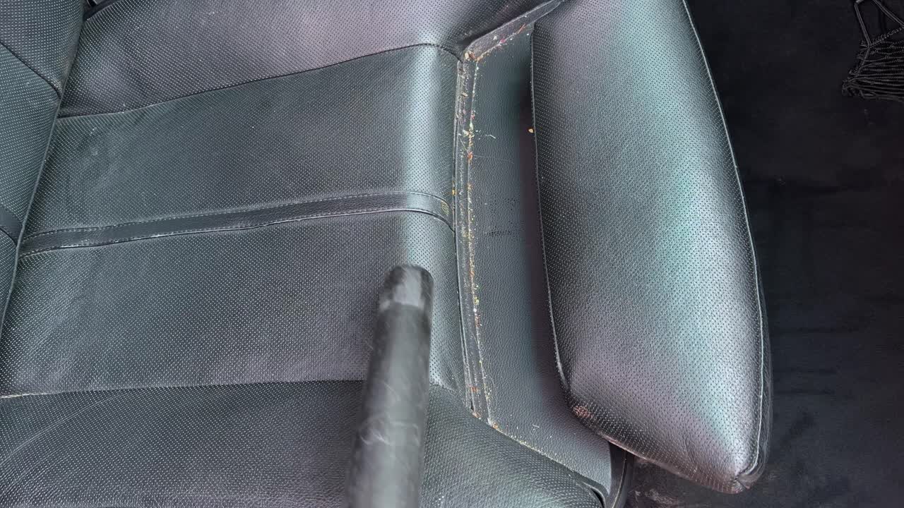 Vacuuming out dirty car floors and black leather seats interior expanding passenger&rsquo;s side leg rest mechanism and cleaning out then back in