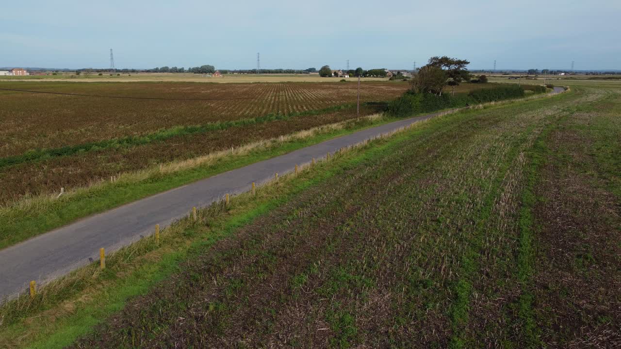 Fixed shot of a countryside road running between open fields in East Sussex under clear daylight