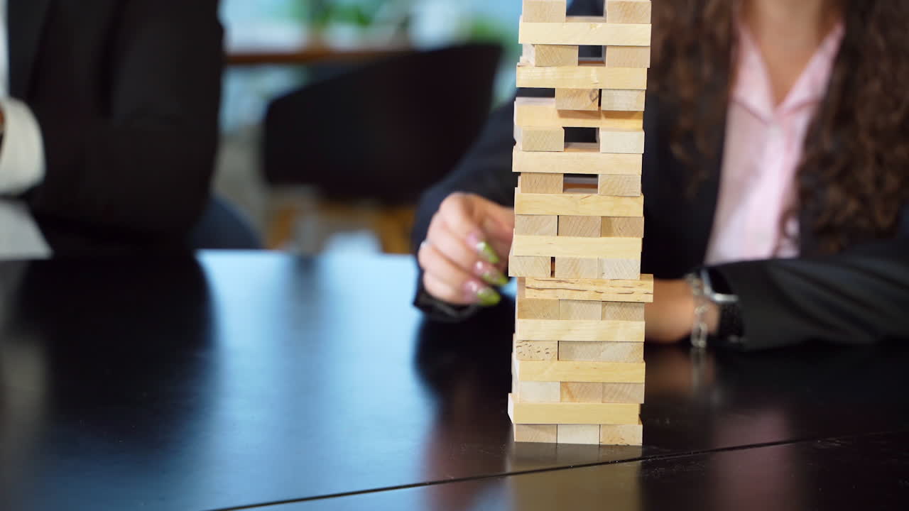 Little wooden bricks stacked up in a pile. People play jenga at the black table. Blurred background.