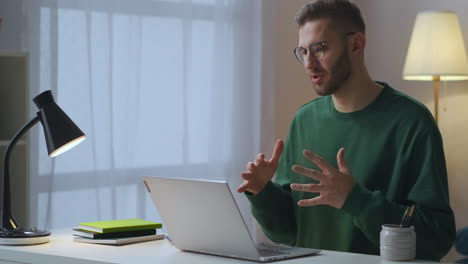 Un-Hombre-Adulto-Saluda-A-Colegas-Y-Socios-En-Una-Reunión-En-Línea-Hablando-Y-Saludando-Con-La-Mano-A-Una-Cámara-Web-Trabajando-Desde-Casa-Con-Tecnología-De-Comunicación-Distante