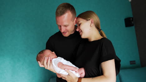 first time parents stand together holding a newborn. couple looks at their baby with adoration.