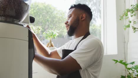 Glücklicher-Afroamerikanischer-Männlicher-Barista,-Der-Im-Café-Kaffee-Mit-Der-Kaffeemaschine-Zubereitet