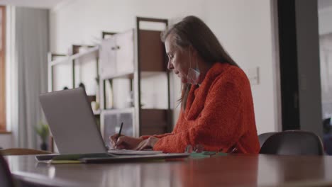 Woman-taking-notes-while-having-a-video-chat-on-her-laptop-at-home