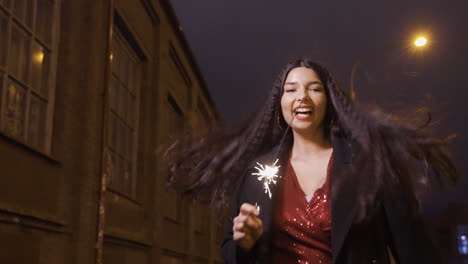 la cámara se enfoca en una joven con ropa elegante sosteniendo una bengala y celebrando la víspera de año nuevo