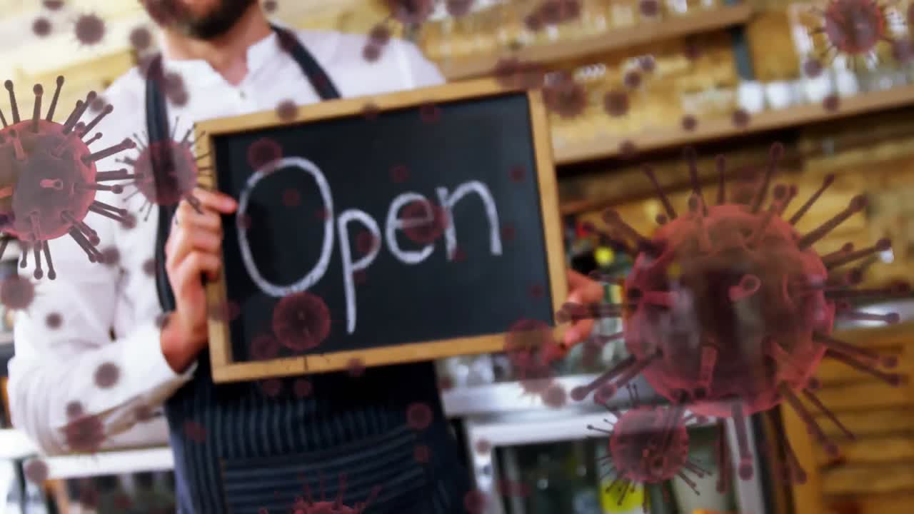 Animation of macro Covid-19 cells floating over happy mixed race male chef holding Open sign