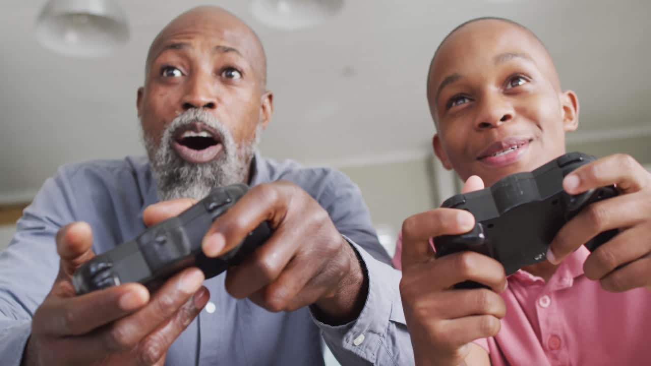video de un padre y un hijo afroamericanos felices jugando videojuegos